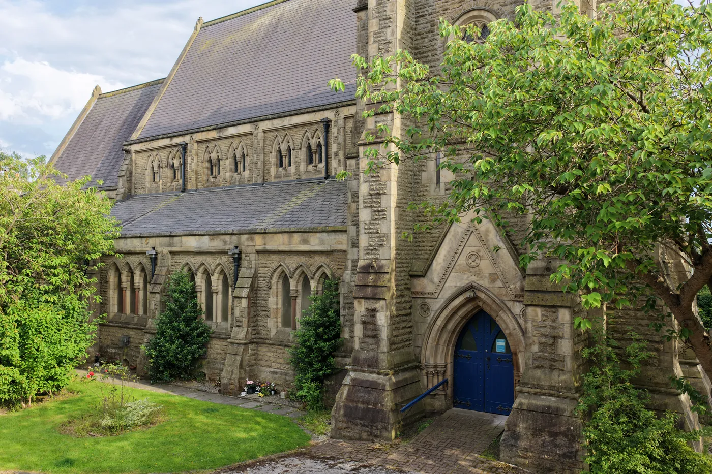 The blue west door of St Thomas beneath its carved stone arch, framed by trees