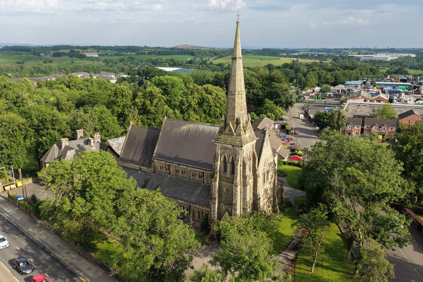 Evening light on St Thomas from the air, the spire above the treetops with the Roch Valley beyond