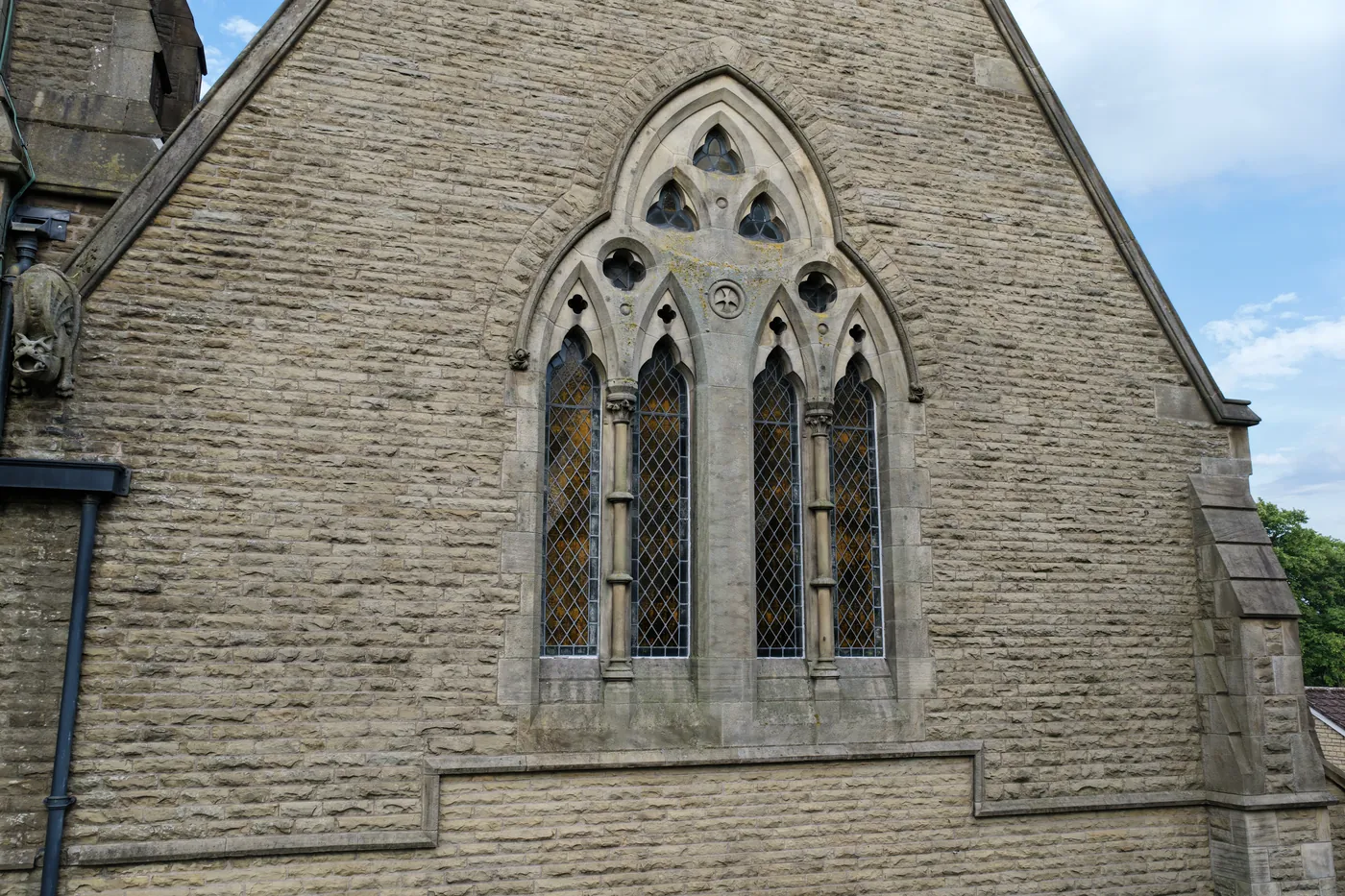 A traceried Gothic window set high in a gable of coursed stone