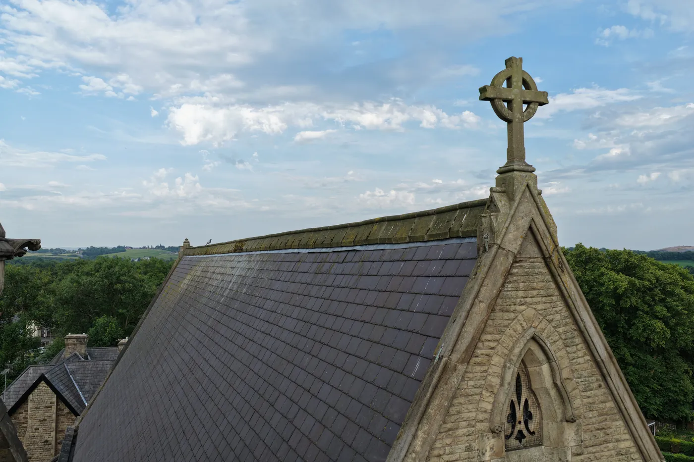 A carved stone cross crowning the gable at the end of the slate roof, seen at roof height