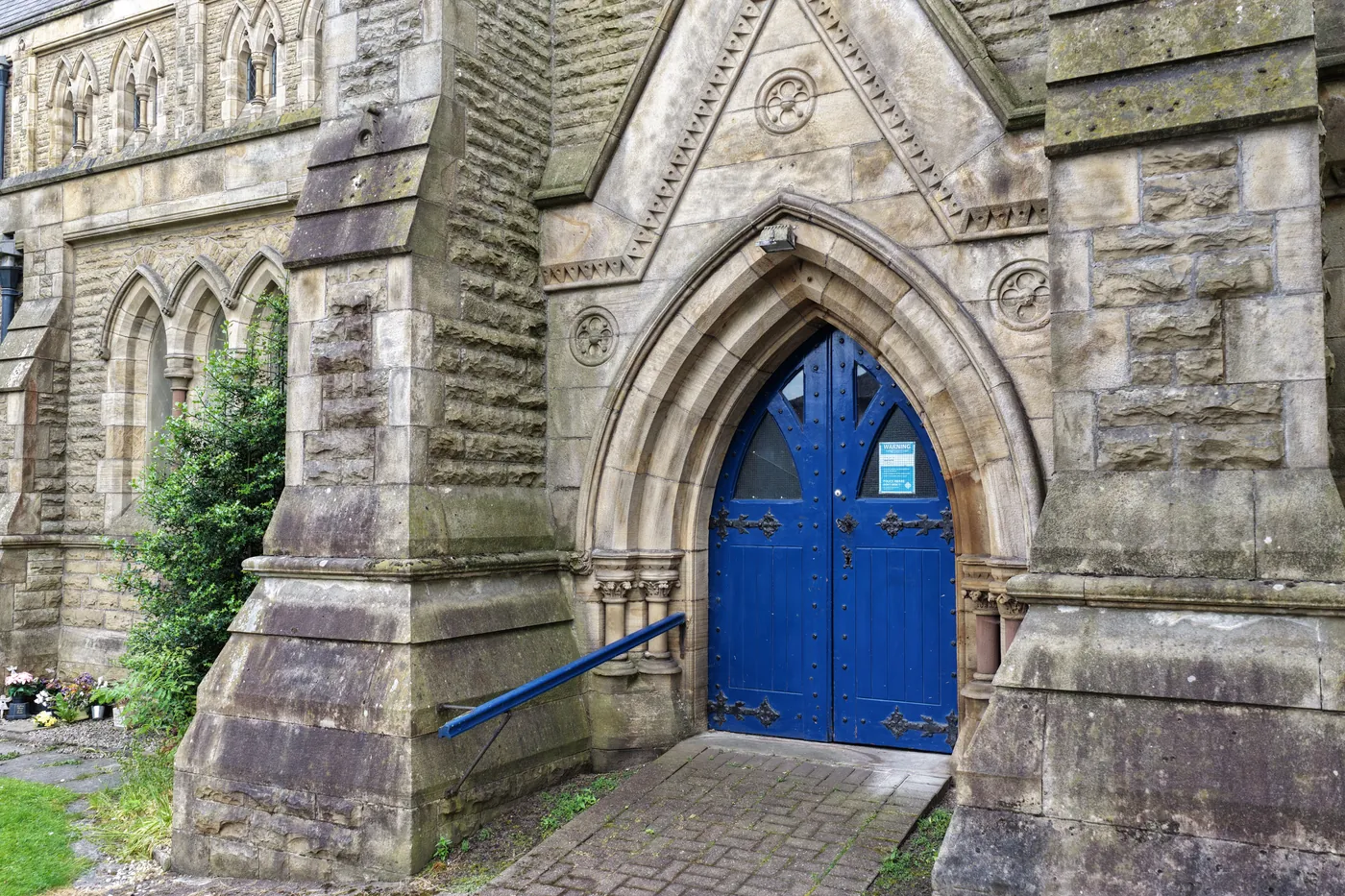 The deep stone porch of St Thomas and its blue double doors, open to the path