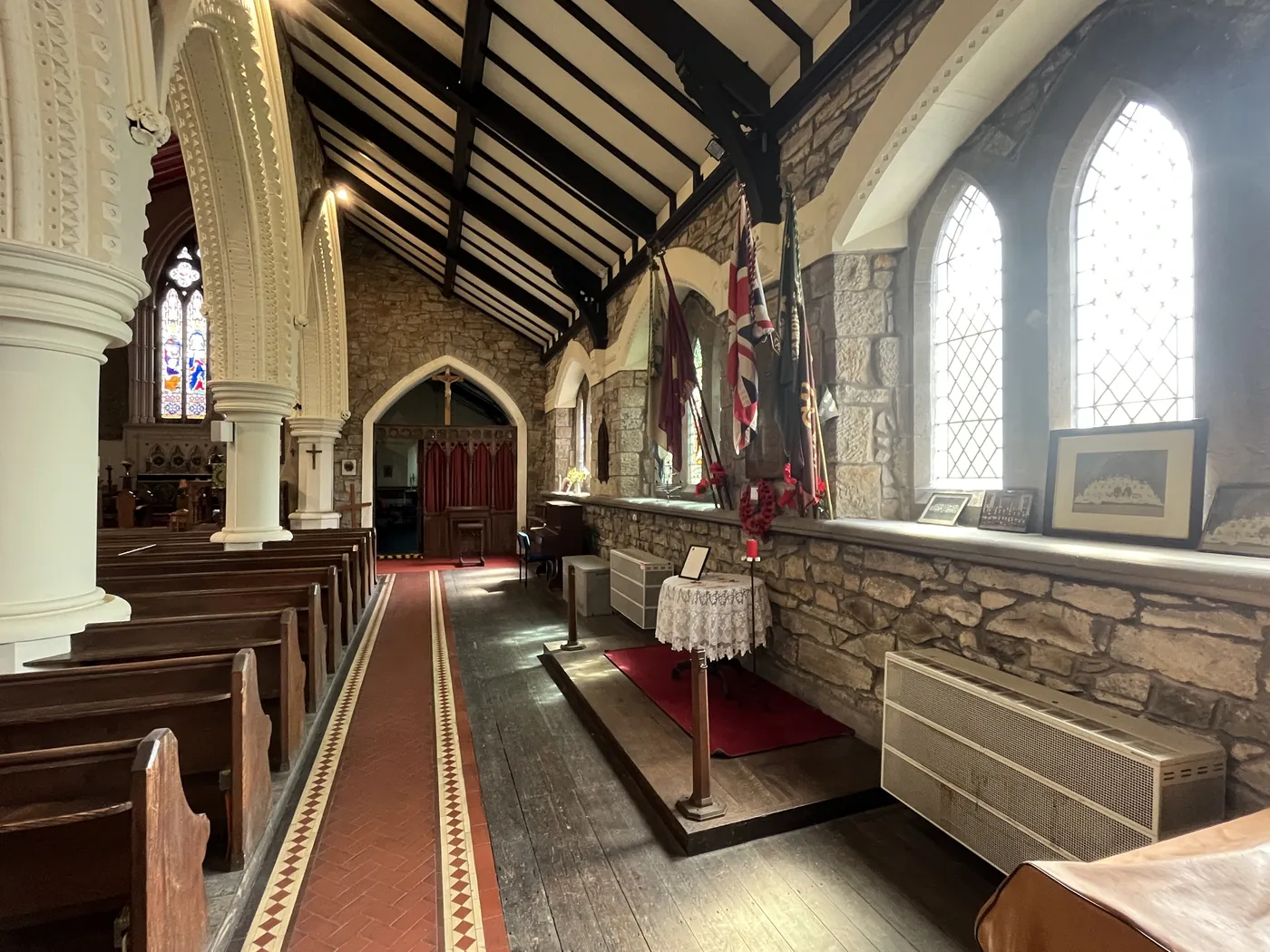 Sunlit side aisle with wooden pews and red tiled floor