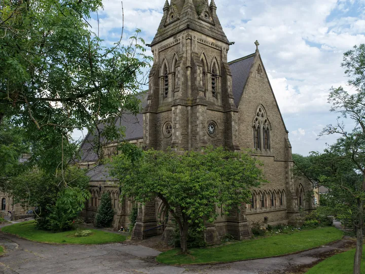 St Thomas from its own churchyard, tower and spire rising above summer trees