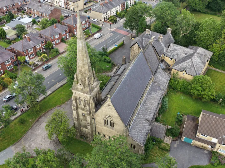 Overhead view of the slate roof, spire and parish buildings of St Thomas beside the road