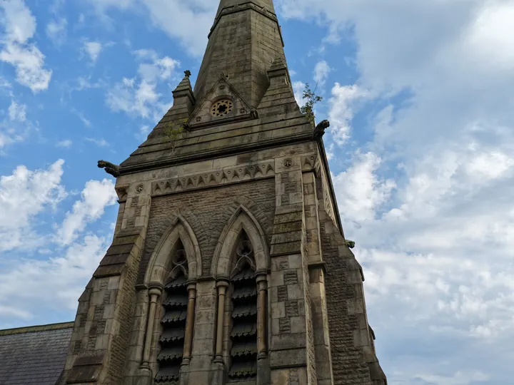 The belfry and spire of St Thomas soaring into a blue, cloud-filled sky