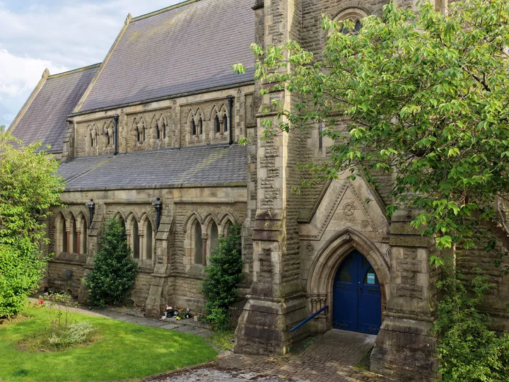 The blue west door of St Thomas beneath its carved stone arch, framed by trees