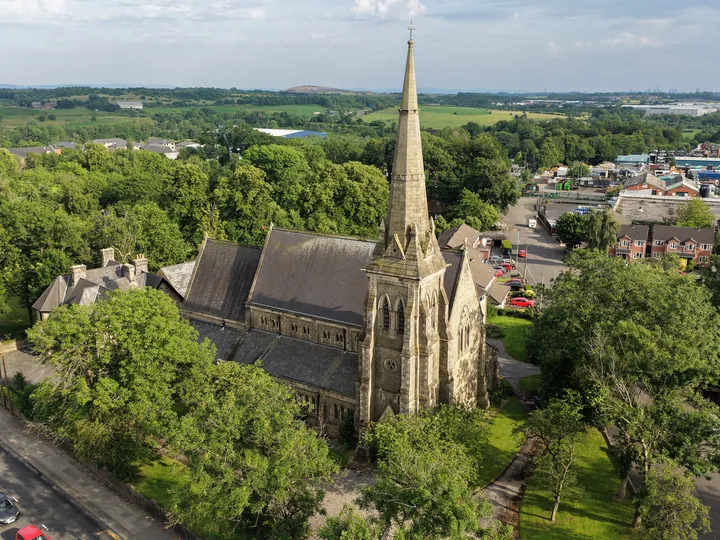 Evening light on St Thomas from the air, the spire above the treetops with the Roch Valley beyond