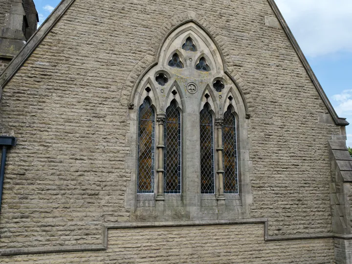 A traceried Gothic window set high in a gable of coursed stone