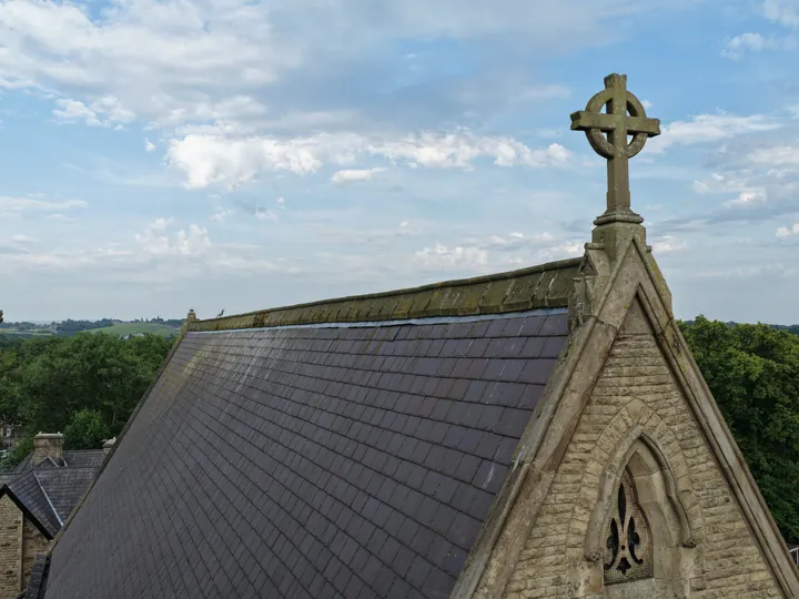 A carved stone cross crowning the gable at the end of the slate roof, seen at roof height