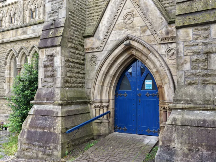 The deep stone porch of St Thomas and its blue double doors, open to the path
