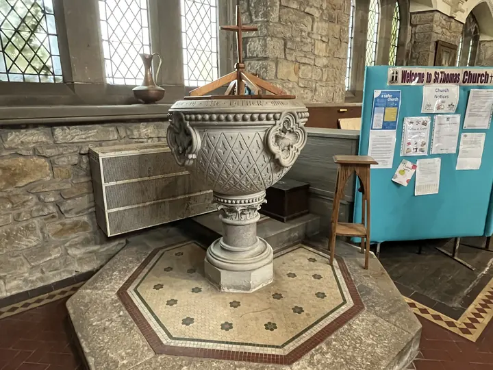 Ornately carved stone baptismal font on a patterned floor