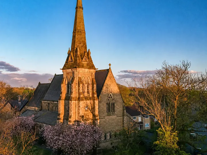 Aerial golden-hour view of St Thomas Church, its tall spire, spring blossom and Roch Valley surroundings